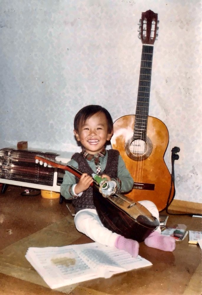 As a child, with a mandolin. He still learns a new piece of music for every novel he writes.